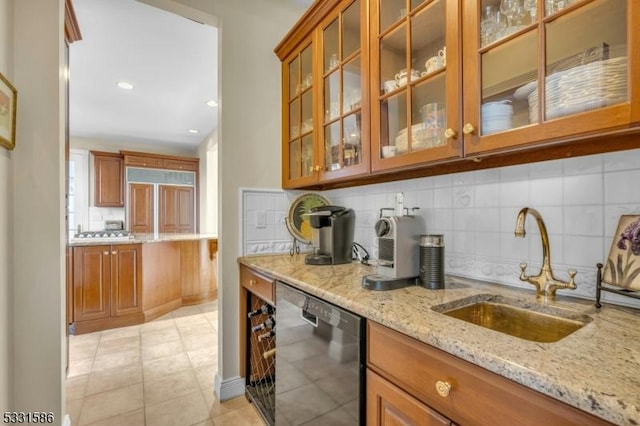 kitchen with light tile patterned floors, backsplash, dishwasher, light stone countertops, and sink