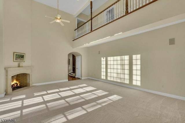 unfurnished living room with ceiling fan, light colored carpet, and a towering ceiling