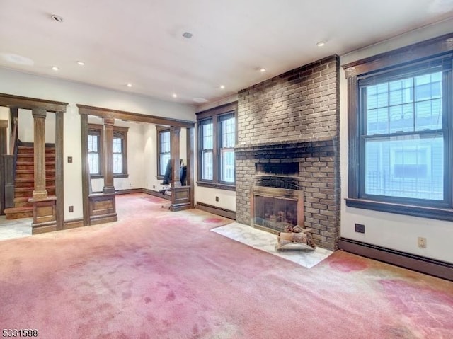 unfurnished living room featuring carpet, plenty of natural light, ornate columns, and a fireplace