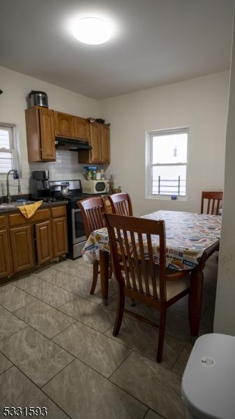 kitchen featuring brown cabinets, dark countertops, a sink, stainless steel range with electric stovetop, and under cabinet range hood