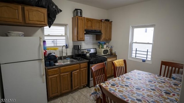 kitchen featuring white appliances, tasteful backsplash, dark countertops, under cabinet range hood, and a sink