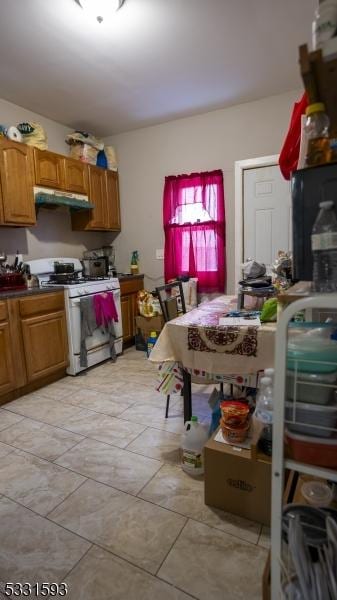 kitchen featuring dark countertops, brown cabinets, white gas stove, and under cabinet range hood