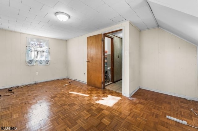 bonus room with dark parquet flooring and vaulted ceiling