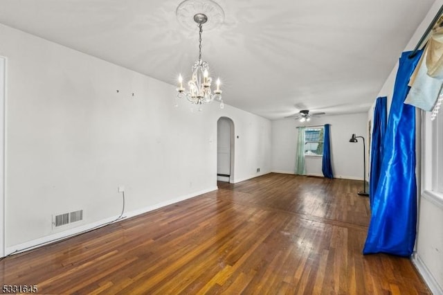 empty room featuring ceiling fan with notable chandelier and dark wood-type flooring