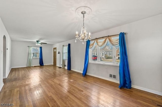 unfurnished room featuring a wealth of natural light, hardwood / wood-style floors, and ceiling fan with notable chandelier