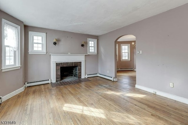 unfurnished living room featuring light wood-type flooring, a baseboard radiator, a brick fireplace, and a healthy amount of sunlight