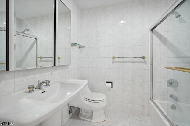 full bathroom with combined bath / shower with glass door, tile patterned flooring, toilet, and tile walls