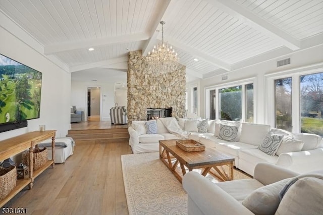 living room featuring lofted ceiling with beams, wooden ceiling, a chandelier, light hardwood / wood-style floors, and a stone fireplace