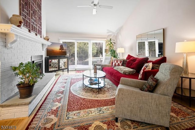 living room with hardwood / wood-style floors, high vaulted ceiling, a brick fireplace, and ceiling fan