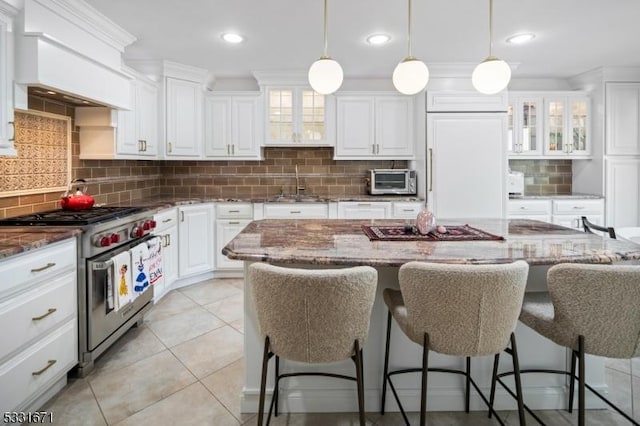 kitchen featuring high quality appliances, decorative light fixtures, white cabinetry, dark stone countertops, and a breakfast bar area