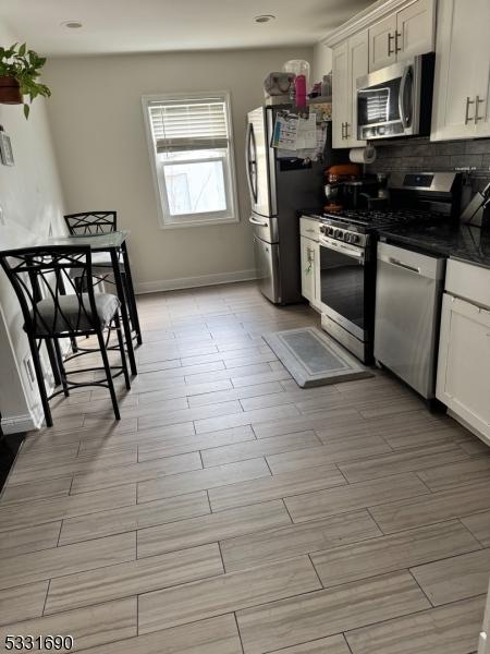 kitchen with backsplash, white cabinetry, and stainless steel appliances