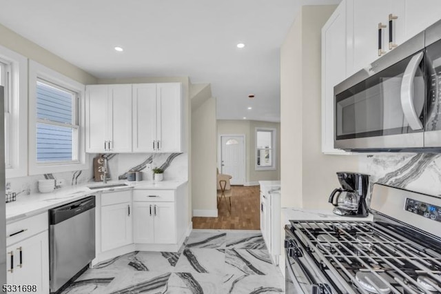 kitchen with white cabinets, stainless steel appliances, light stone countertops, and sink