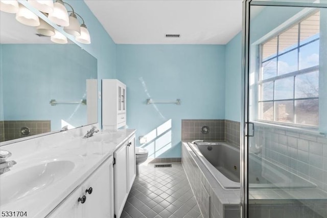 bathroom with a relaxing tiled tub, toilet, vanity, and tile patterned flooring