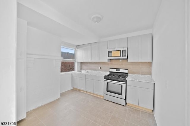 kitchen featuring stainless steel gas stove, light stone countertops, sink, and tasteful backsplash