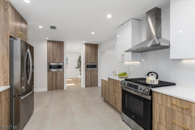 kitchen featuring decorative backsplash, stainless steel appliances, white cabinetry, and wall chimney range hood