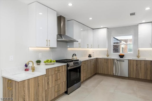 kitchen with sink, white cabinets, stainless steel appliances, and wall chimney range hood