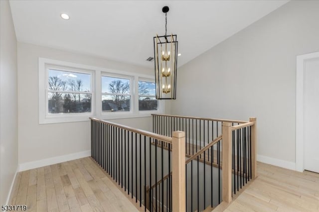 corridor featuring lofted ceiling, light hardwood / wood-style flooring, and a notable chandelier