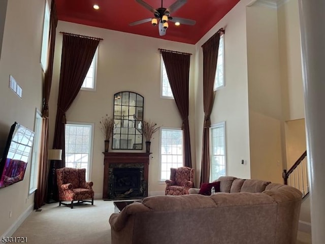 carpeted living room featuring ceiling fan, a fireplace, and a high ceiling