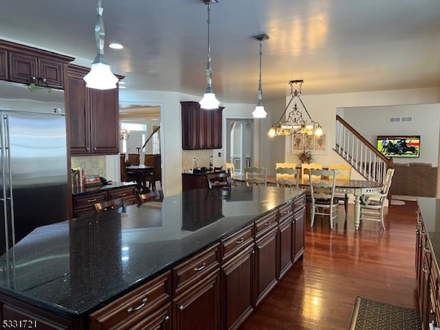 kitchen with pendant lighting, built in refrigerator, dark hardwood / wood-style floors, dark stone countertops, and a kitchen island