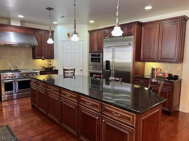 kitchen with a center island, wall chimney range hood, dark stone counters, pendant lighting, and high quality appliances