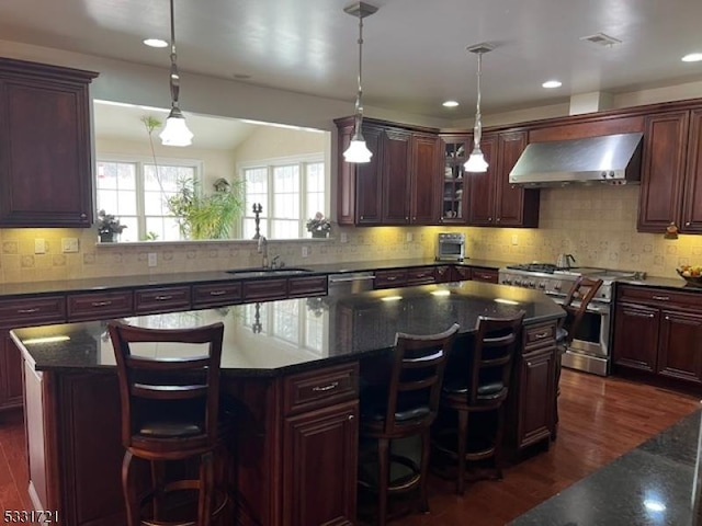 kitchen with a center island, wall chimney exhaust hood, stainless steel appliances, sink, and decorative light fixtures