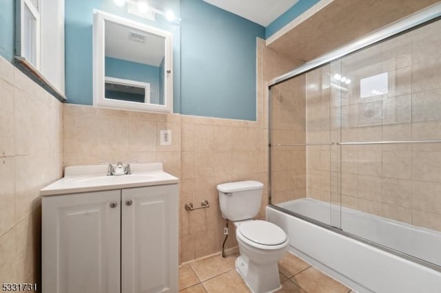 full bathroom featuring enclosed tub / shower combo, tile patterned floors, toilet, vanity, and tile walls