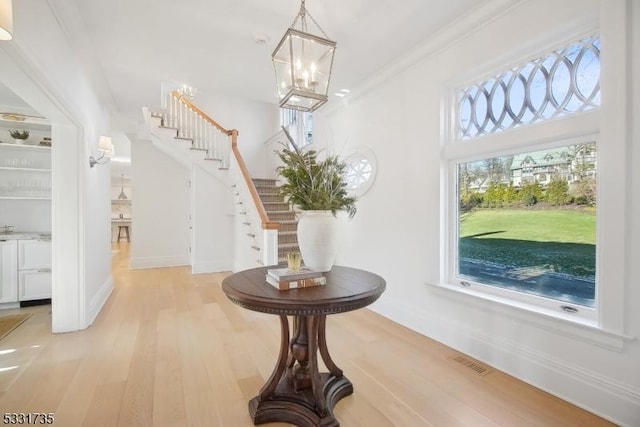 foyer featuring light hardwood / wood-style floors, crown molding, and a chandelier