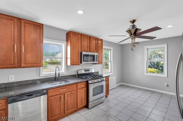 kitchen featuring radiator, dark stone countertops, appliances with stainless steel finishes, ceiling fan, and sink