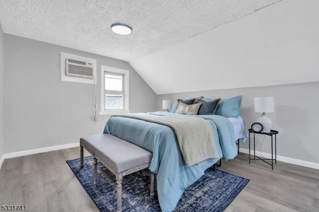 bedroom with a textured ceiling, a wall mounted air conditioner, vaulted ceiling, and wood-type flooring