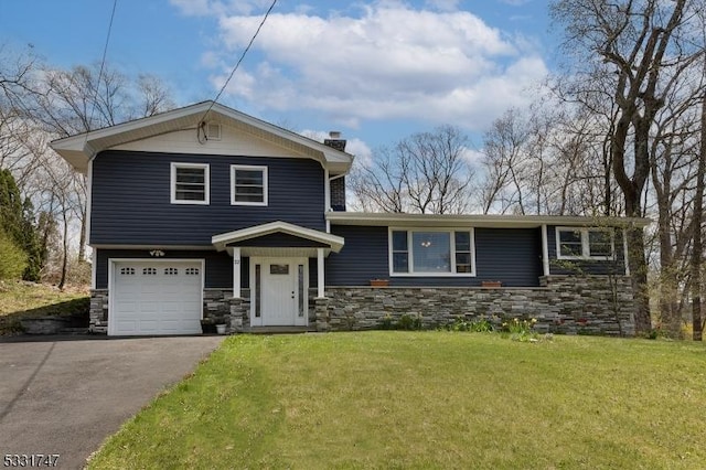 tri-level home featuring driveway, a chimney, a front yard, an attached garage, and stone siding