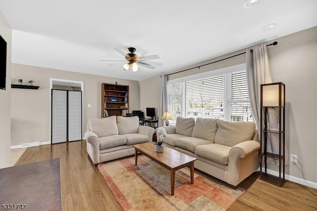 living area featuring baseboards, a ceiling fan, and light wood-style flooring