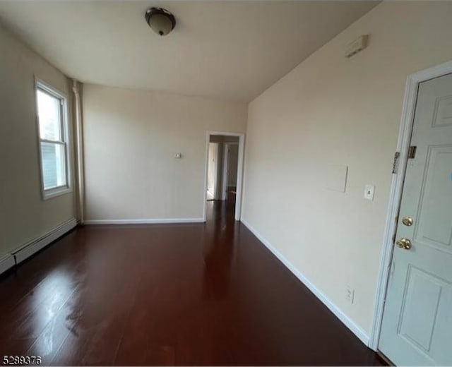 spare room featuring baseboard heating and dark wood-type flooring