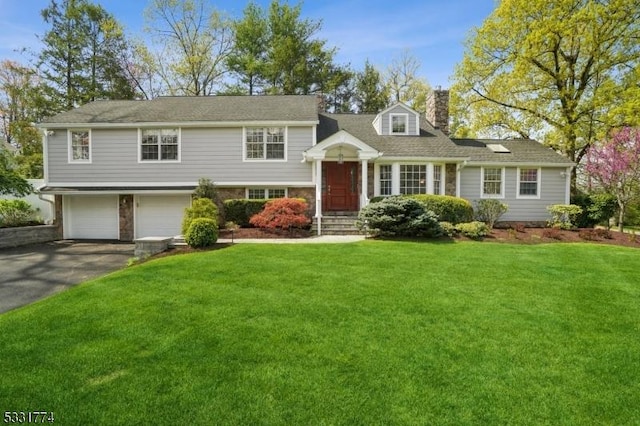 tri-level home featuring a chimney, an attached garage, aphalt driveway, and a front yard