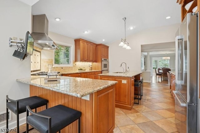 kitchen featuring wall chimney range hood, a sink, stainless steel appliances, a peninsula, and a wealth of natural light