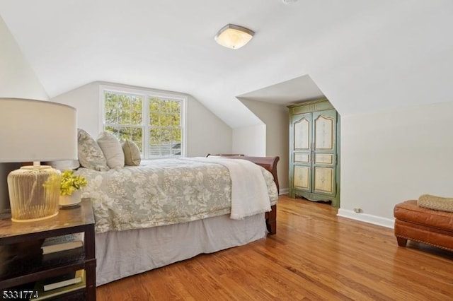 bedroom featuring baseboards, wood finished floors, and vaulted ceiling