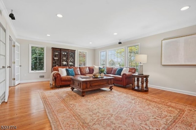 living room featuring light wood-style floors, plenty of natural light, visible vents, and crown molding