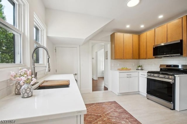 kitchen with light wood finished floors, stainless steel appliances, backsplash, and light countertops