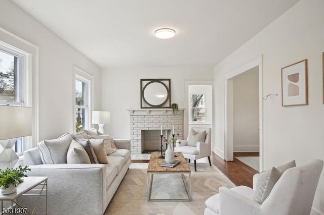 living area featuring a brick fireplace, baseboards, and wood finished floors