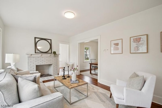 living room with baseboards, a brick fireplace, and wood finished floors