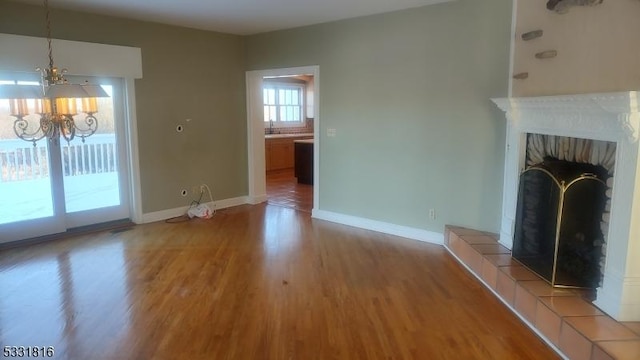 unfurnished living room featuring a tile fireplace, hardwood / wood-style flooring, and an inviting chandelier