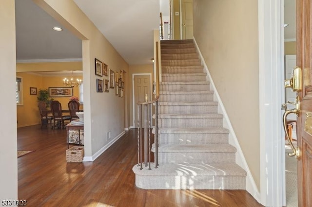 staircase featuring a notable chandelier, hardwood / wood-style floors, and crown molding