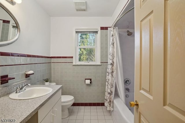 full bathroom featuring tile patterned flooring, tile walls, toilet, shower / bath combo with shower curtain, and vanity