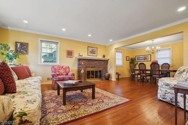 living room featuring a brick fireplace, an inviting chandelier, hardwood / wood-style flooring, and crown molding