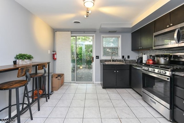 kitchen featuring sink, light tile patterned floors, dark stone counters, and appliances with stainless steel finishes