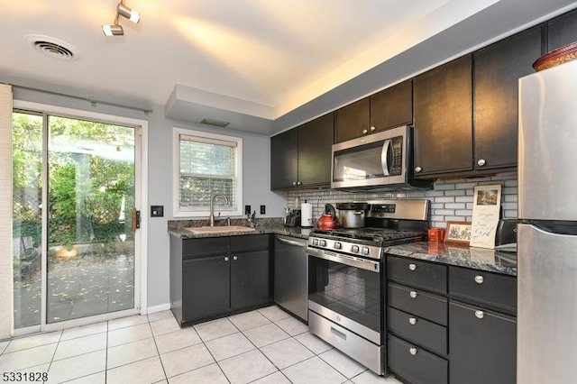 kitchen featuring dark brown cabinetry, sink, dark stone countertops, light tile patterned flooring, and appliances with stainless steel finishes