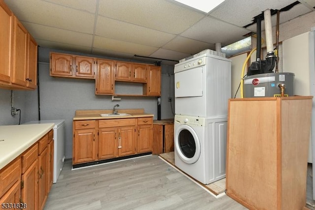 laundry room with sink, cabinets, water heater, stacked washer and dryer, and light hardwood / wood-style floors