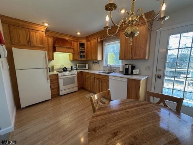 kitchen featuring custom exhaust hood, white appliances, pendant lighting, a chandelier, and light hardwood / wood-style floors