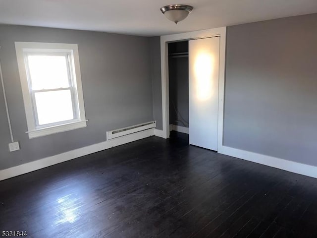 unfurnished bedroom featuring dark wood-type flooring, a closet, and a baseboard heating unit