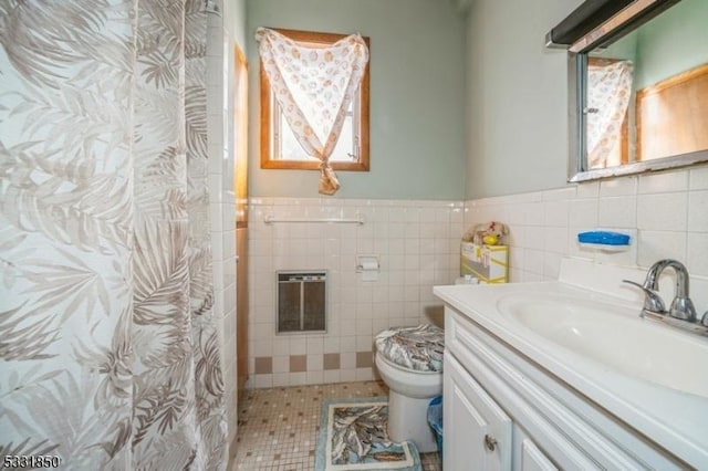 bathroom featuring tile patterned floors, vanity, heating unit, tile walls, and toilet