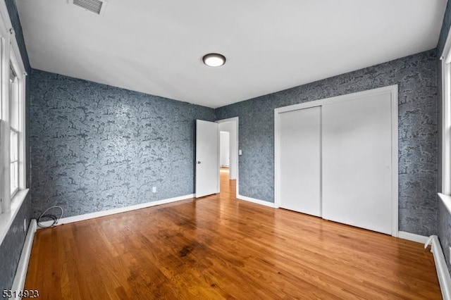 unfurnished bedroom with a baseboard heating unit, a closet, and wood-type flooring